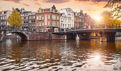 Panoramic view at the bridges on the channel in Amsterdam, Netherlands. Dutch houses above river Amstel. Famous landmark in old european city. Autumn fall sunset landscape.