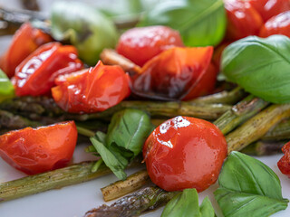 Wholesome roasted asparagus dish with cherry tomatoes and basil on a white plate, light and full of Mediterranean flavor.

