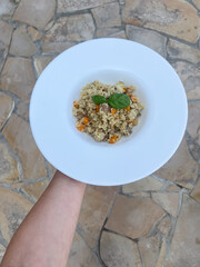 Colorful couscous with vegetables served in white plate, garnished with fresh basil.