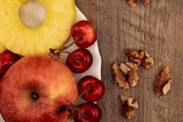 A red apple, pineapple rings, and red cherries are neatly arranged, with scattered walnuts adding a...