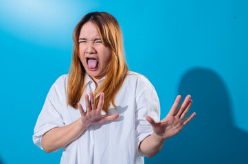 Asian woman in a white shirt reacting in disgust and fear, sticking out her tongue and raising her...
