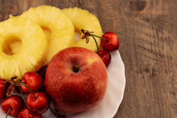 pineapple rings, red cherries, and a red and yellow apple are artfully arranged, healthy and appealing produce. Ideal for themes of wholesome eating, summer refreshments, and natural food beauty