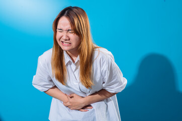 Asian woman in white shirt holding her stomach in pain with a tense facial expression, eyes closed...