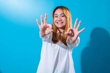 Asian woman with long straight hair in white shirt makes double OK hand gestures while smiling and...