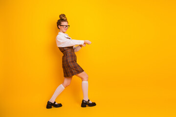 Young student in plaid uniform posing playfully against a vibrant yellow background, expressing joy...