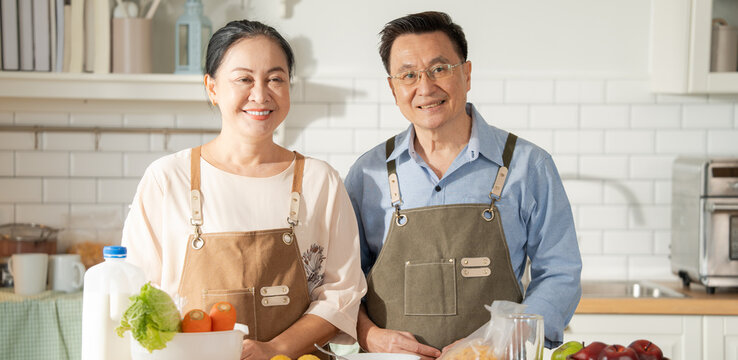 Asian senior couple in apron standing at the cooking counter in the kitchen. Happy moment of grandparents in the morning preparing for breakfast