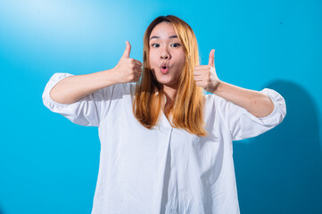 Asian woman with long straight hair in white shirt smiles and enthusiastically gives double thumbs...