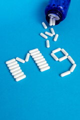 Dietary supplements. White pills arranged in the Mg symbol and a blue bottle from which pills are poured out on a blue background with space for text.