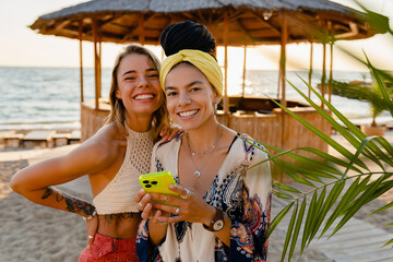 girls friends together having fun on vacation on summer beach using smartphone