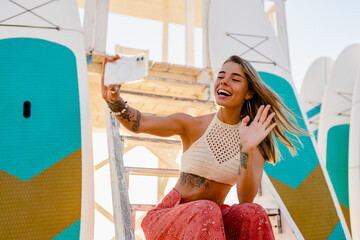 beautifil blond woman posing on summer beach in sunny weather using smartphone