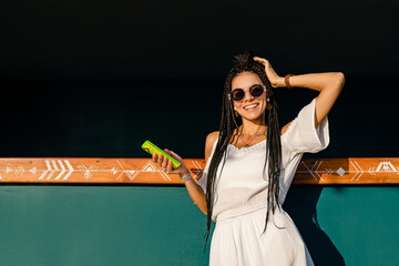 beautiful tanned smiling skinny woman posing on summer tropical vacation in white trendy dress using smartphone