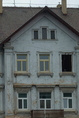 The image depicts an aging residential building that displays peeling paint, a broken window, and other signs of wear, showcasing its historical significance and the passage of time