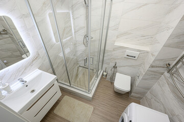 Modern bathroom featuring a glass shower, white sink vanity, toilet, and washing machine. The space...