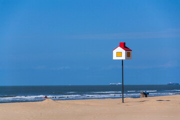 Wooden model of a house with a red roof on a pole on a sandy beach, coastal village De Haan, West Flanders, Belgium