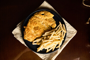 Pork or chicken Milanese, with french frieson plate on wooden table. Mediterranean, latin american food.