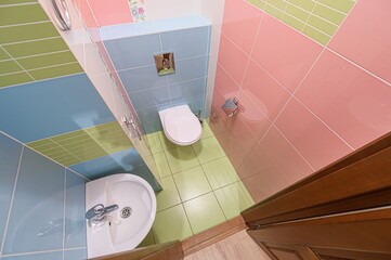 Bright bathroom with colorful tiles: pink, blue, green. Includes a toilet, sink, and wooden door