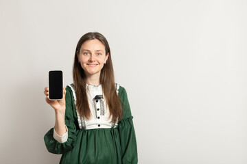 A woman with long hair stands in a well-lit room, smiling at the camera as she holds up a...