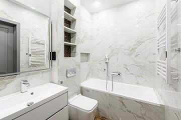 bright, modern bathroom features white marble tiles, a sleek vanity, a toilet, and a bathtub. ...