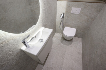 modern bathroom with gray tile walls and floor features a white toilet, sink, and round mirror
