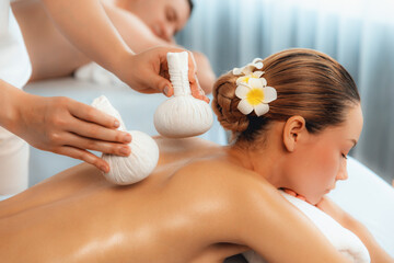Hot herbal ball spa massage body treatment, masseur gently compresses herb bag on couple customer...