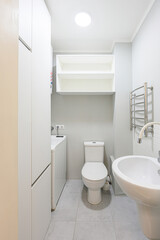 small, modern bathroom with a toilet, sink, washing machine, and storage. The color scheme is primarily white and grey, with a simple and clean design