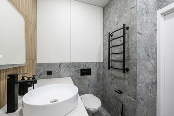 Modern bathroom features gray marble tiles, a white sink, black fixtures, and minimalist design for...