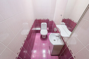 small, tiled bathroom features a toilet, sink, and mirror. The decor uses a pink and white color...