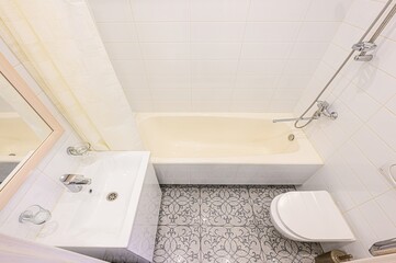 bright bathroom featuring white tiles, a cream-colored tub, a white sink, and a patterned floor