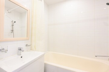 Clean, bright bathroom featuring white tiles, a sink with a chrome faucet, a mirror, and a bathtub