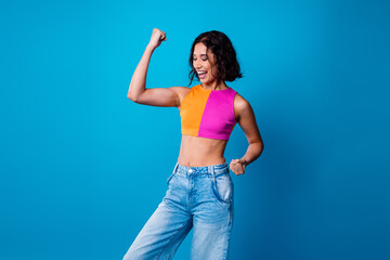 Cheerful young woman in stylish top and denim expressing happiness against blue background with...