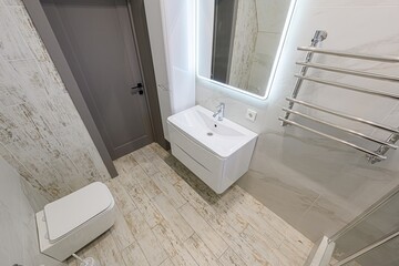 Modern bathroom with white sink, LED mirror, heated towel rack, gray door, and wood-look tile. Minimalist design