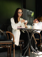 Stylish woman enjoying coffee outdoors. freelancer relaxing at summer cafe