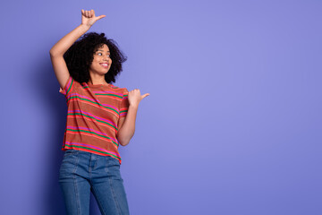 Happy young woman with curly hair in colorful t-shirt gesturing on purple background, expressing...