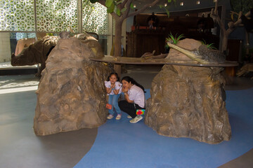 A playful moment of a young girl and her mother pretending to hide from a wild animal exhibit in the water animal section of a museum. engaging experience of family museum visits. pretend fear and fun