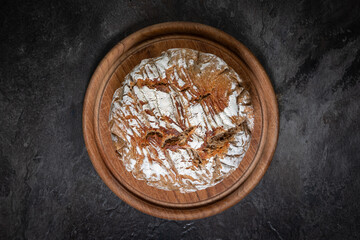 Round rustic bread on wooden board and dark slate background, top view

