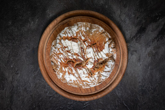 Round rustic bread on wooden board and dark slate background, top view


