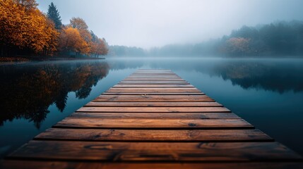 Wooden dock extends into a calm lake on a misty autumn morning.