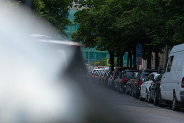 A vibrant street scene showcases parked cars neatly aligned on both sides of the road, with tall...