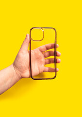 Hand holding a transparent smartphone case against a vibrant yellow background, showcasing modern design and functionality for mobile device protection and style enhancement