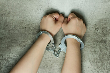 Hands in handcuffs isolated on gray concrete background. Concept of arrest, crime, punishment, law...