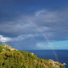 A rainbow leading from the Ionic sea over Taormina in front of a dramatic cloudy and stormy sky 
