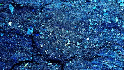 Close-up, textured abstract blue background. Features a rough, granular surface with cracks and...