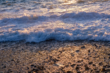Wave over the pebble beach with sunlight. Shimmering reflections of sunlight on the water. The...