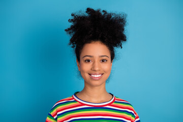 Young woman wearing colorful striped t-shirt smiling confidently against a teal blue background...