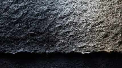 Close up of a textured dark gray surface with a gradient of light and shadow across the surface