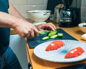 Side View of Male Hands Cutting Fresh Green Cucumber Next to Plate of Sliced Tomatoes