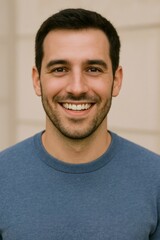 Obraz premium Cheerful young male smiling warmly, wearing blue casual sweater, standing against neutral background, embodying friendly professional demeanor
