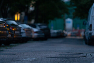 A tranquil street scene that features parked cars lined along a dimly lit road, effectively showcasing the beauty of an urban environment during the enchanting hour of dusk