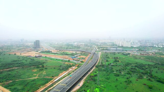 aerial drone sideways trucking shot showing traffic on elevated Dwarka expressway with green fields around and skyscraper buildings in distance