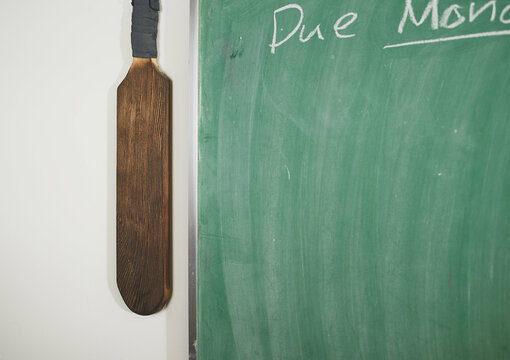 Vintage Wooden Paddle Hanging by Classroom Chalkboard - Traditional School Discipline Concept